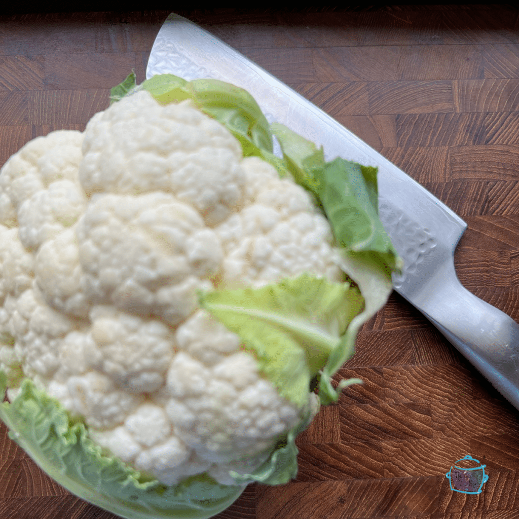 A whole head of cauliflower with a knife sitting next to it.