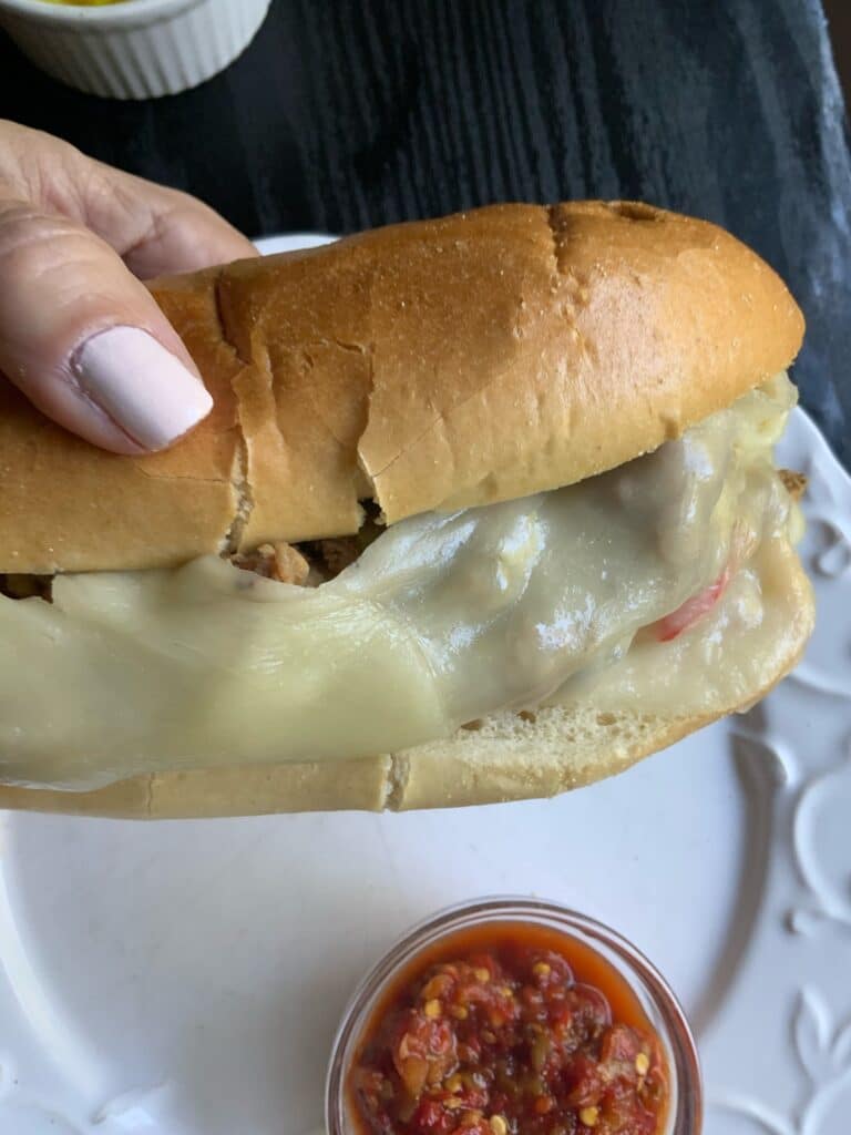 A hand holding a whole cheesesteak sandwich