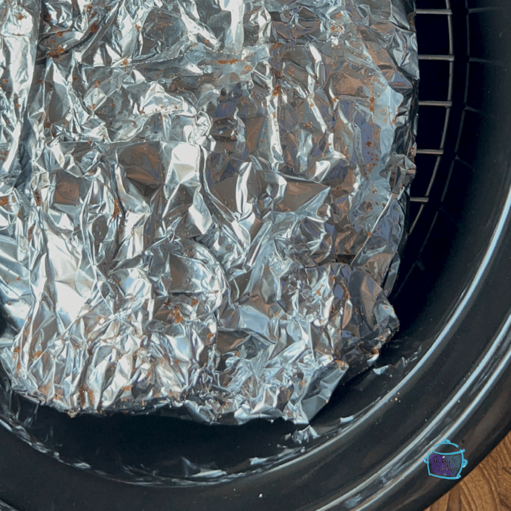 Pastrami wrapped in foil on rack in slow cooker