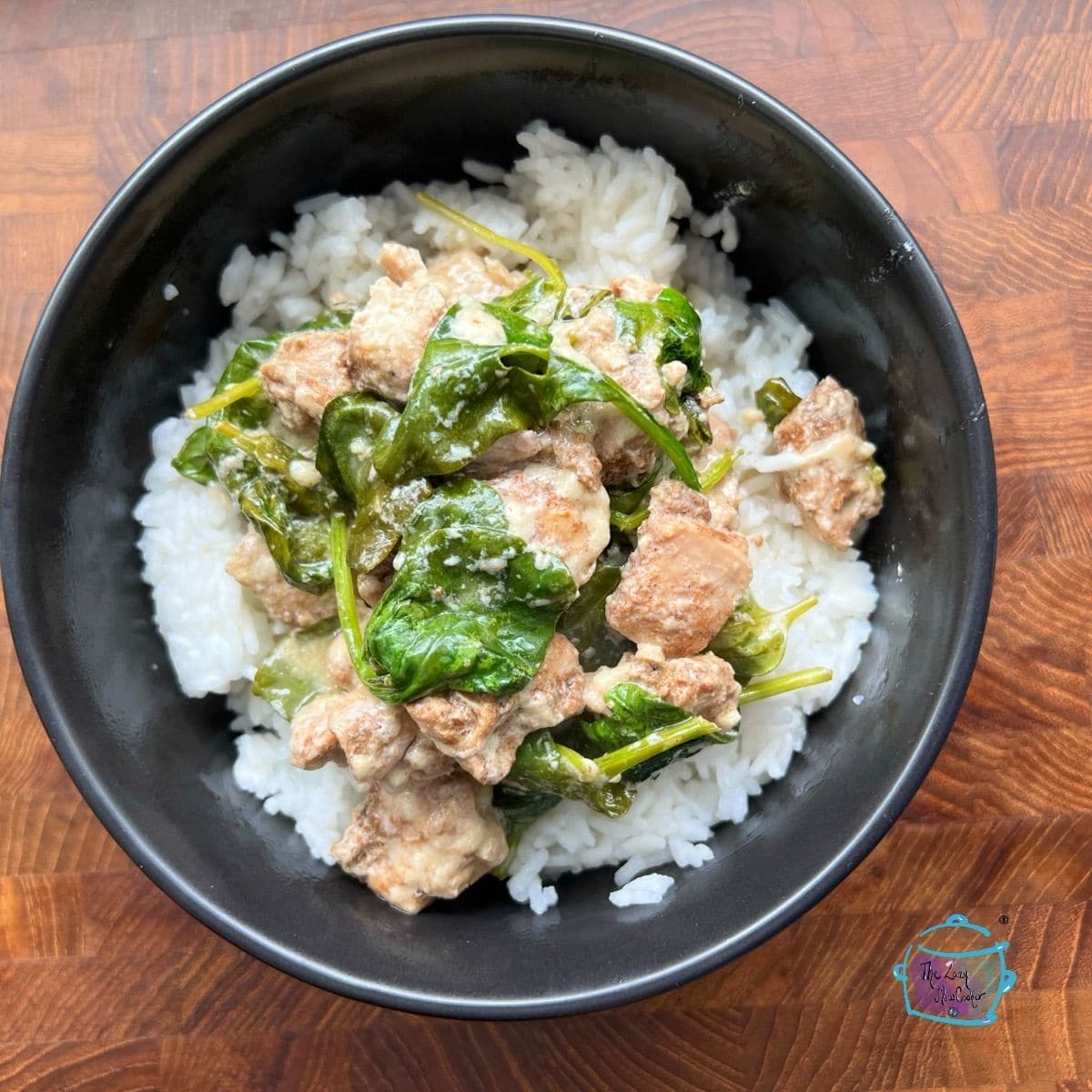 A round black bowl filled with creamy lemon chicken and spinach over rice