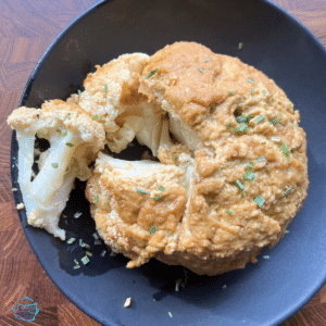 Whole cauliflower cooked with dijon parmesan topping with a wedge cut out of it.