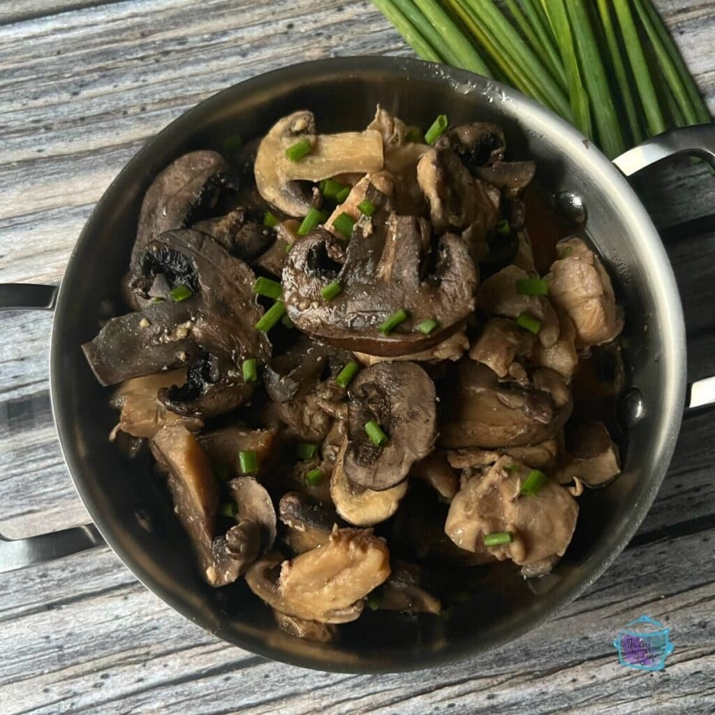 looking down on a pot full of braised mushroom and chicken pieces with fresh chives