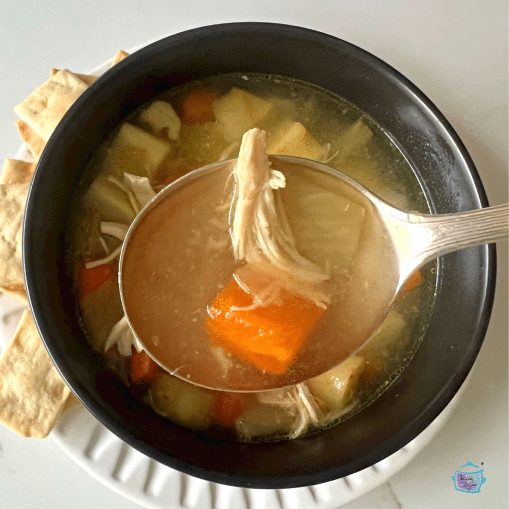 Finished chicken soup in a black bowl with some chicken pieces on a spoon