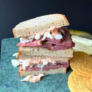 slow cooked pastrami on rye bread with cole slaw and Russian dressing dripping down. chips on side