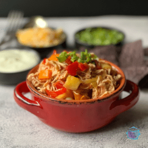 A side view of a red bowl filled with shredded chicken, mango and pepper chunks