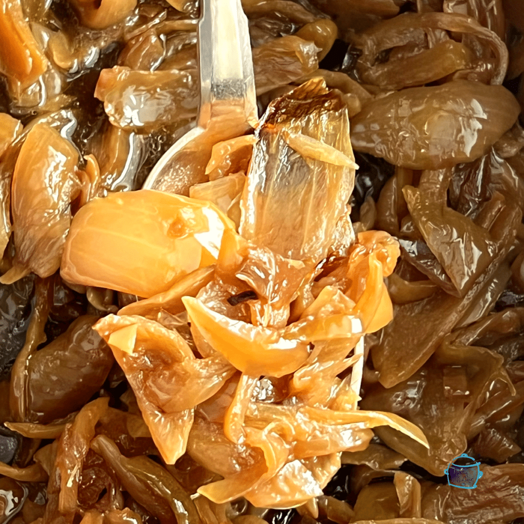 Slow cooked caramelized onions on a spoon with more onions in the background