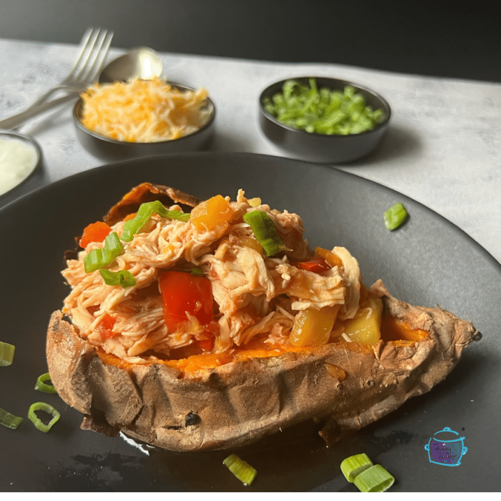 A sweet potato stuffed with mango chicken on a black plate with some cheese and green onion in the background