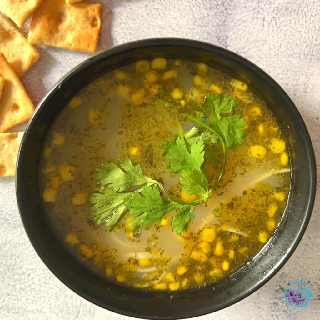 looking down on a bowl of chicken soup with corn kernels floating in it. topped with some fresh basil