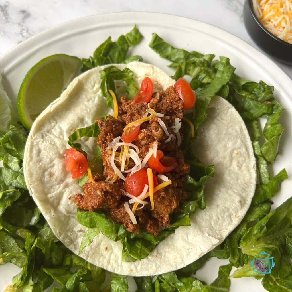 Turkey taco ingredients laying on a soft taco shell out of slow cooker