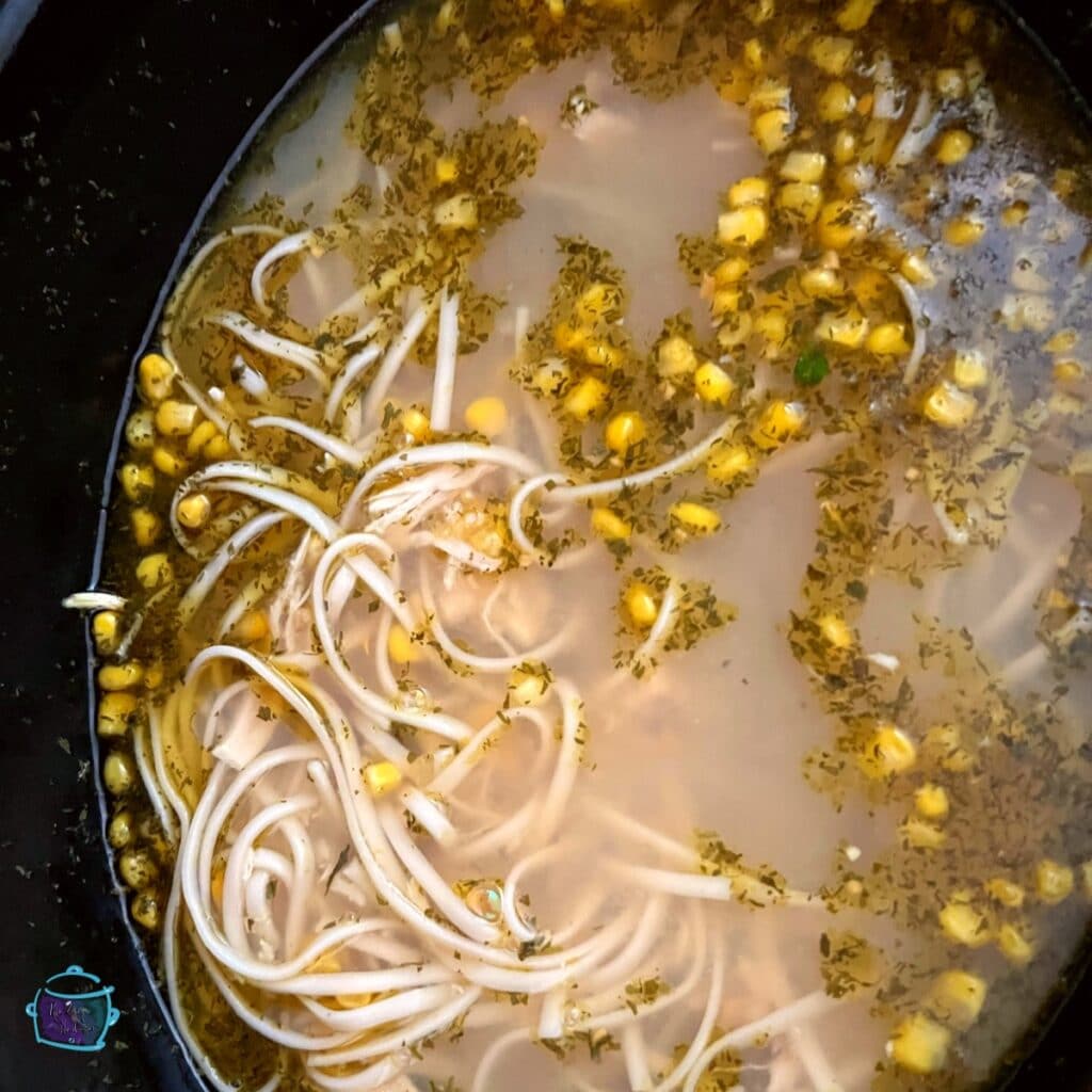 looking down on a crockpot full of chicken and corn soup with noodles