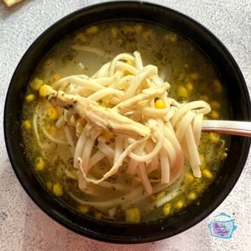 looking down on a spoonful of noodles held over a bowl of chicken soup with corn