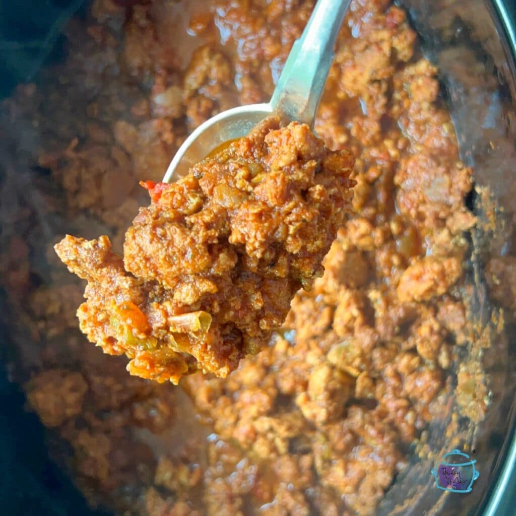 Close up of turkey taco meat held on a spoon in front of crockpot