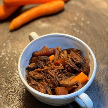 Shredded roast and carrots in a bowl with raw carrots in the background