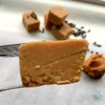 Side view of a piece of fudge held by tongs with more fudge blurred in background