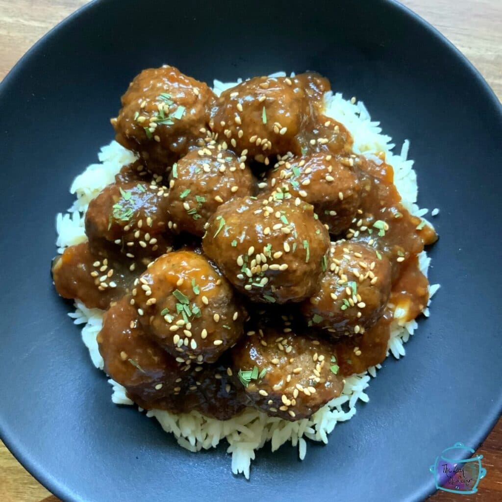 meatballs in a black bowl over rice topped with sesame seeds