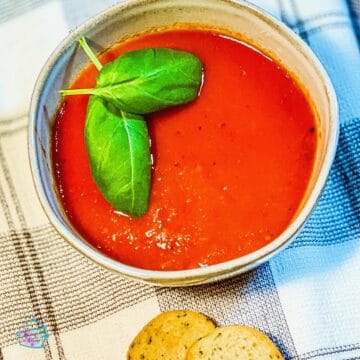 A bowl of tomato soup with basil leaves on top