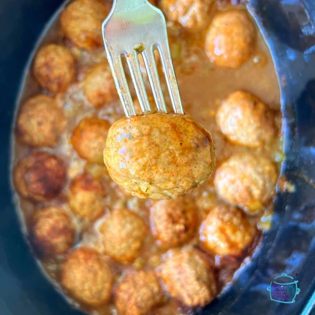 enchilada meatballs after being slow cooked. One is held on a fork