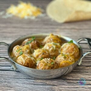 a round metal pan filled with creamy turkey enchiladameatballs topped with cheese