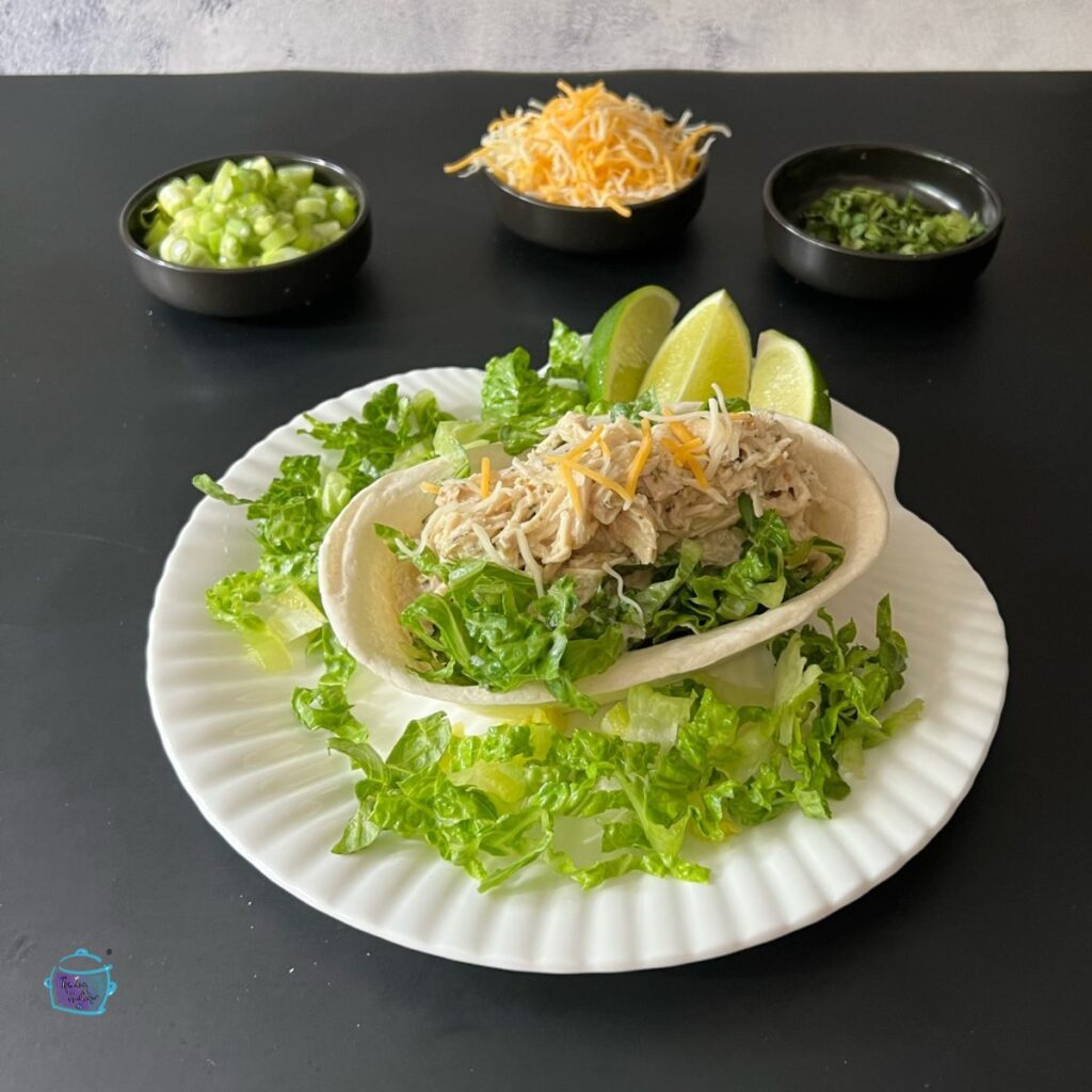 a tortilla bowl filled with shredded salsa verde chicken, lettuce and cheese