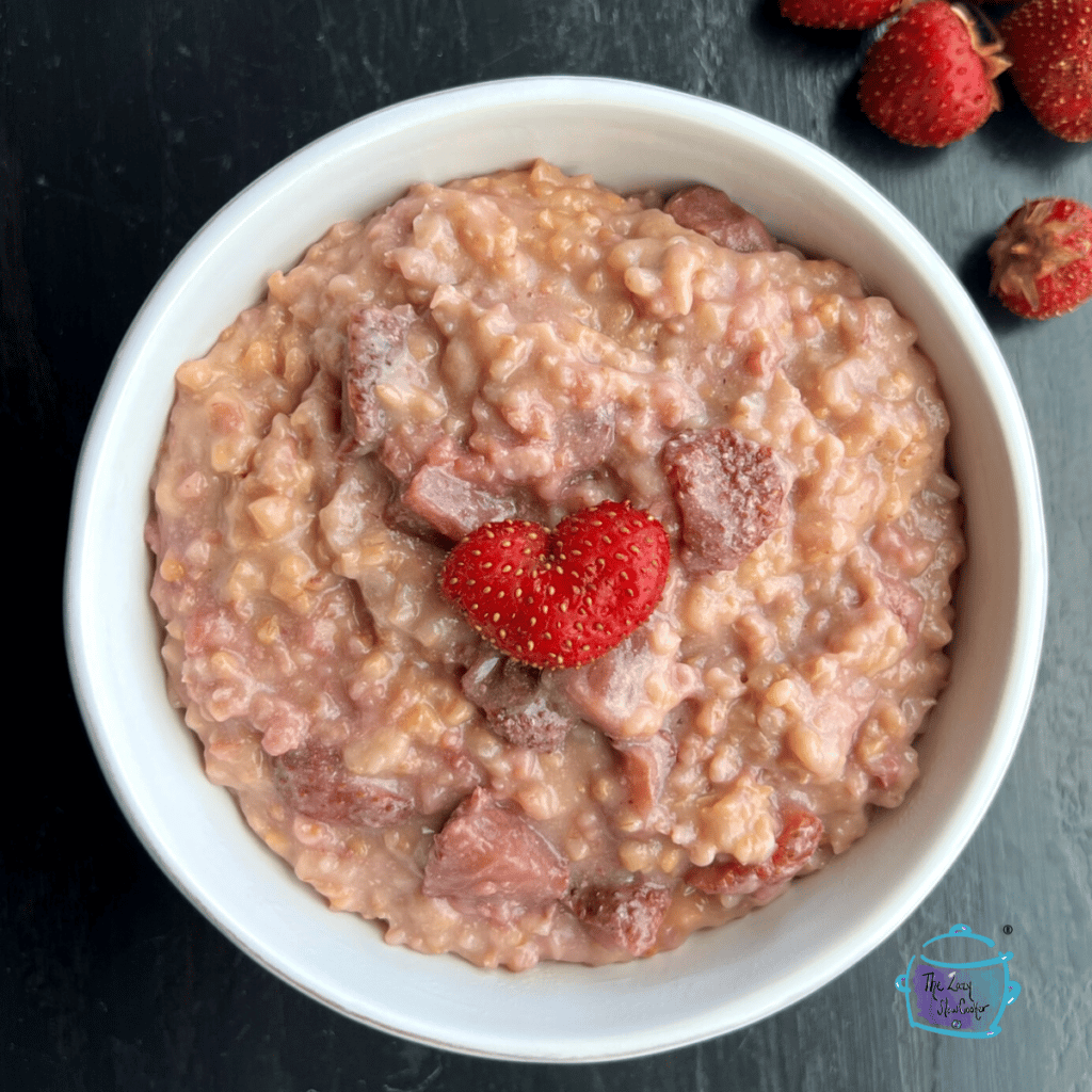 looking down on a bowl full of strawberry and cream oatmeal in a bowl with a hear shaped berry on top