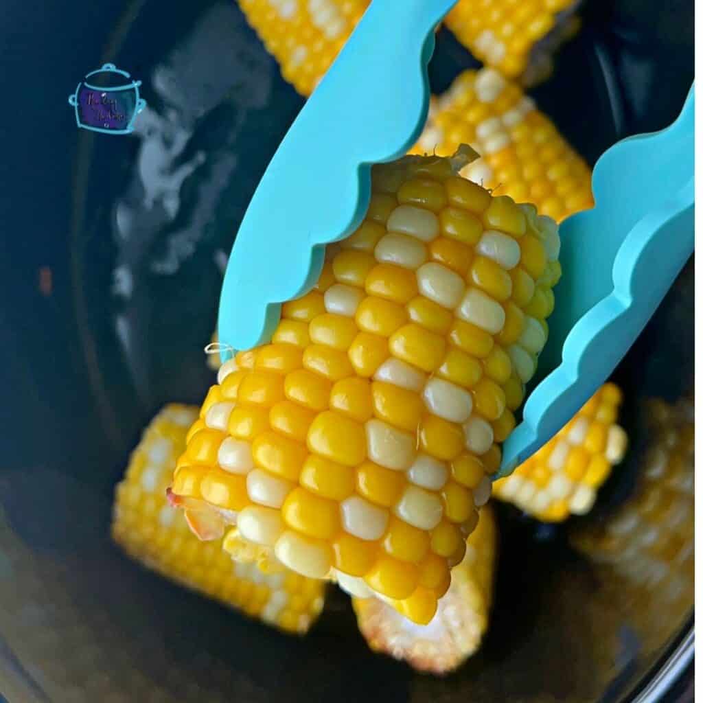 half an ear of slow cooked corn held with tongs