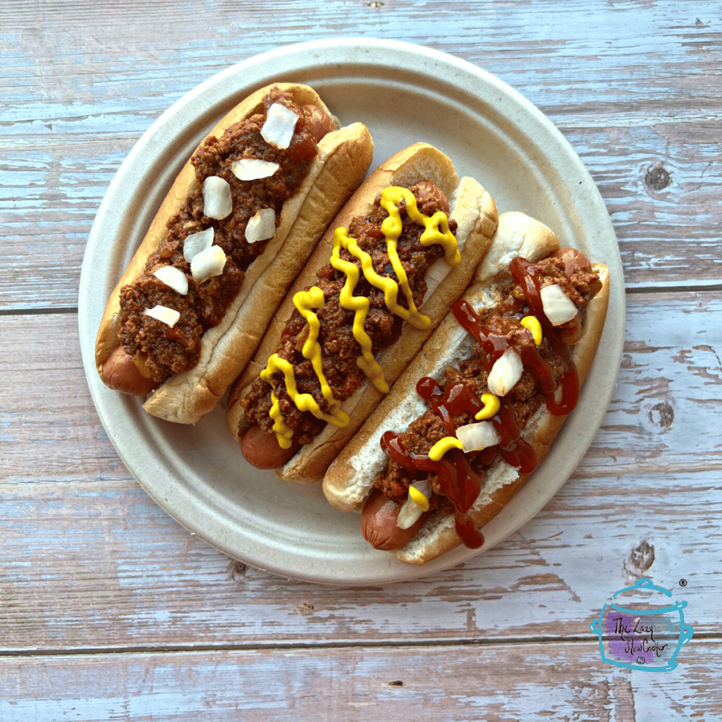 three hot dogs on a plate topped with chili and other toppings