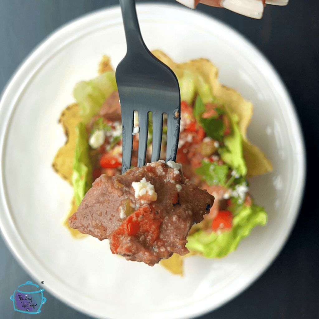 slow cooker carne picada on a fork with a bowl full of it in the background