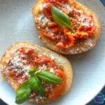 close up of two pieces of toast covered with slow cooked tomatoes and garlic some fresh basil and grated parmesan cheese