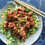 A plate with shredded cabbage topped with slow cooker bang bang chicken