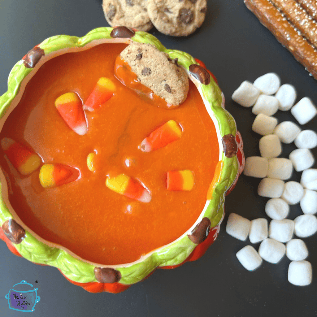 halloween dessert dip made in slow cooker out of candy corn wit a cookin in it and other items laying around ready to dip