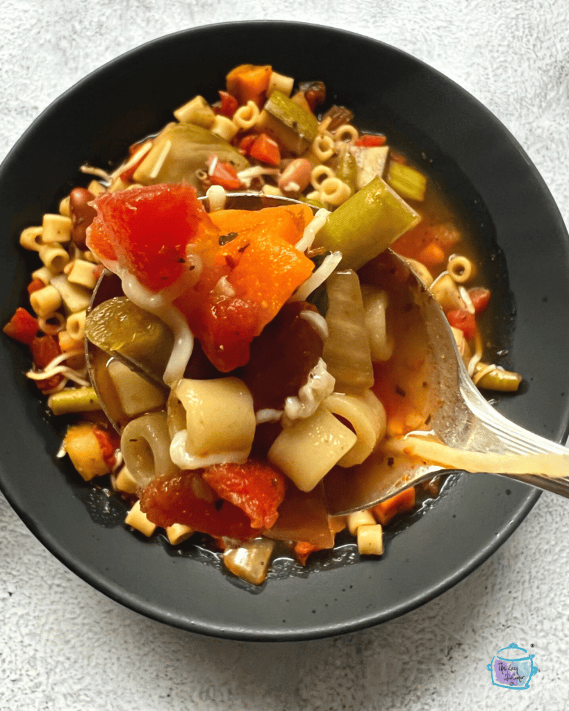 a spoonful of slow cooker minestrone soup held over a bowl