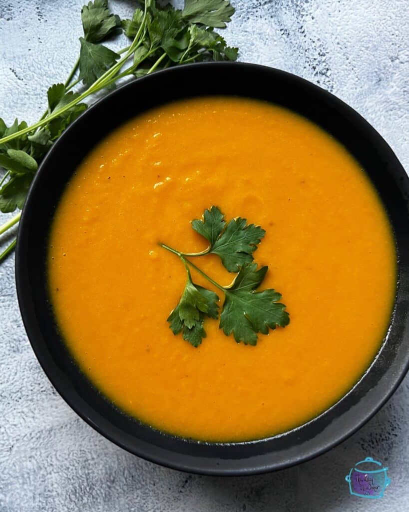 looking down on a bowl of carrot ginger soup topped with parsley