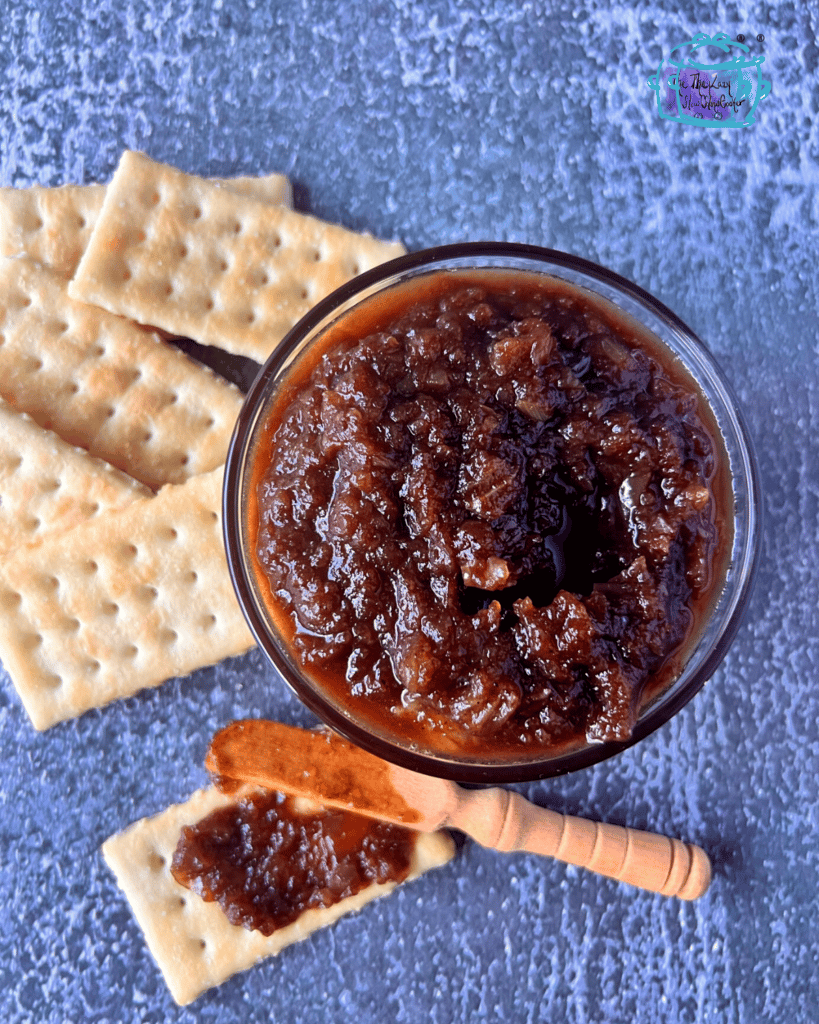 maple onion jam after finished slow cooking in a bowl with crackers and a wooden spreading knife