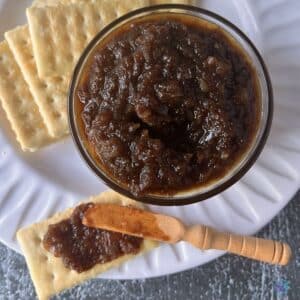 maple onion jam after finished slow cooking in a bowl with crackers and a wooden spreading knife