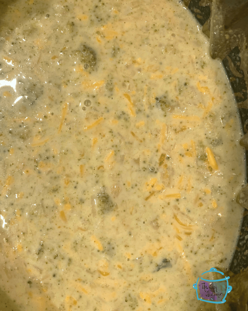 A crockpot full of cooked cheddar and broccoli soup ingredients before using immersion blender
