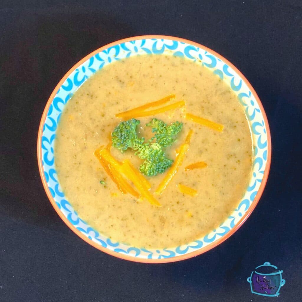 a bowl of slow cooker cheddar and broccoli soup topped with fresh broccoli