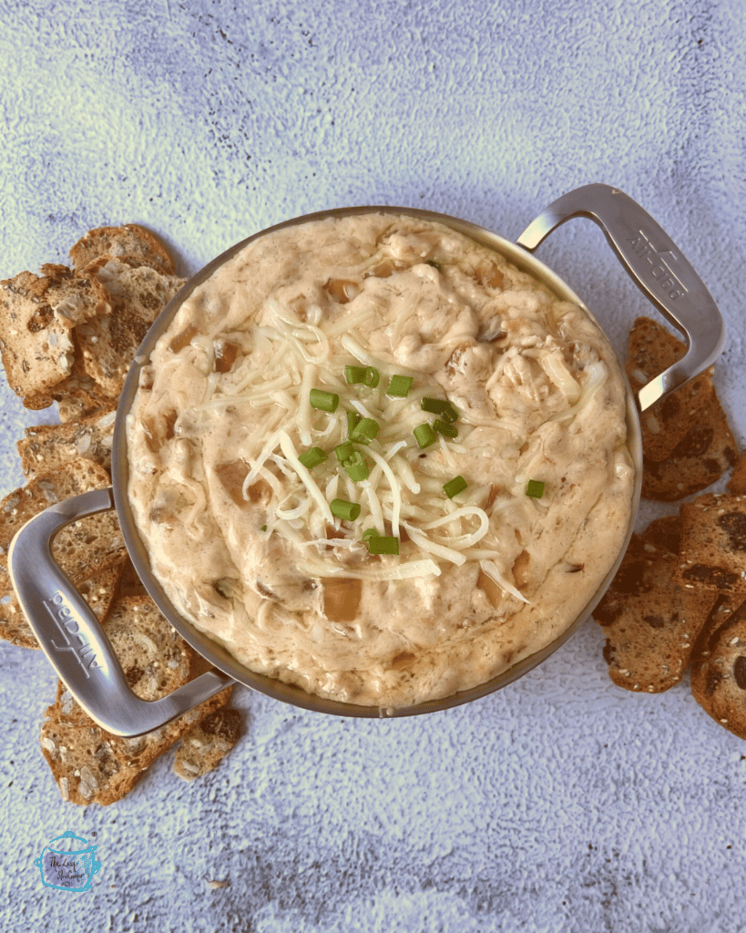 looking down on a sliver bowl filled with slow cooker onion and cheese dip with pretzels on the side