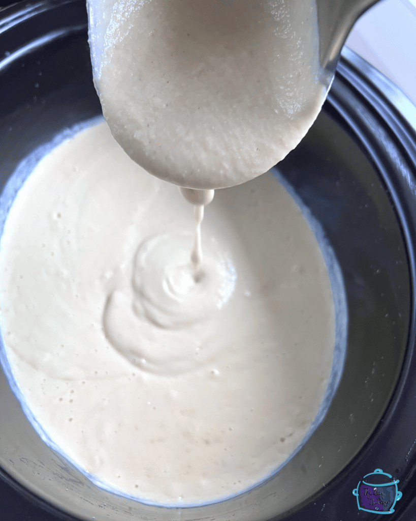 creamy cauliflower soup dripping off a ladle into a sow cooker.