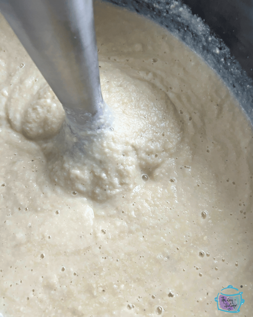 crockpot full of cauliflower soup with an immersion blender in it