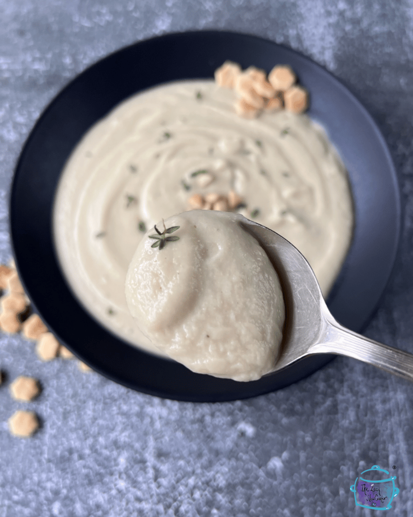 a spoon full of creamy dairy free cauliflower soup being held over a bowl of the same