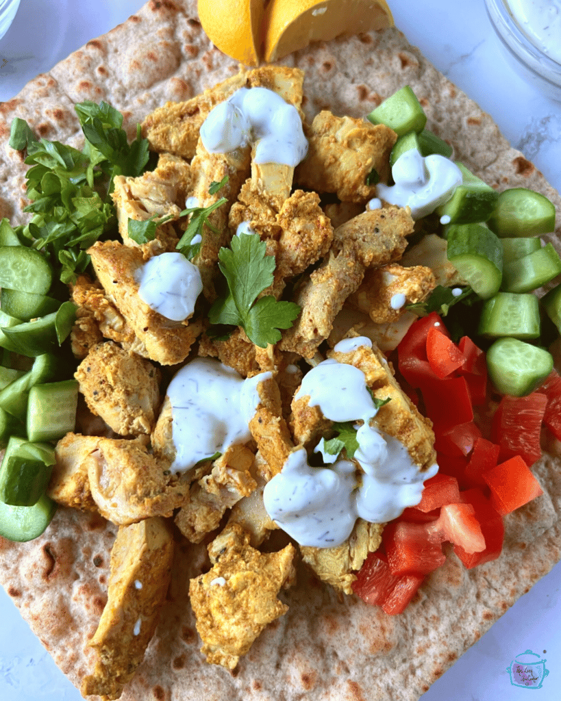 Looking down on a flat bread with slow cooker chicken shawarma surrounded by veggies an topped with white sauce