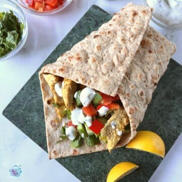 A wrap filled with chicken shawarma and veggies and sauce