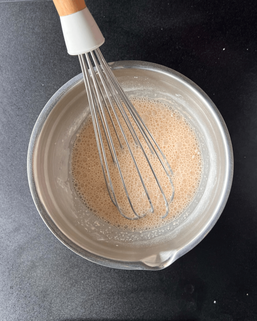 a whisk in a bowl with evaporated milk and flour in it
