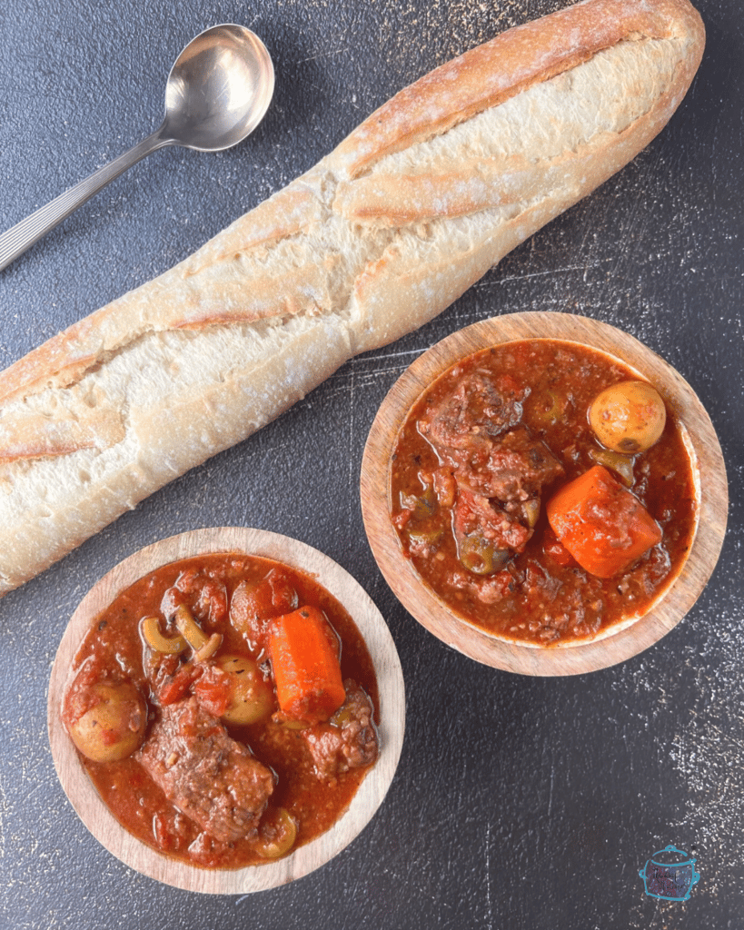 two bowls filled with Spanish slow cooker stew and a crusty roll