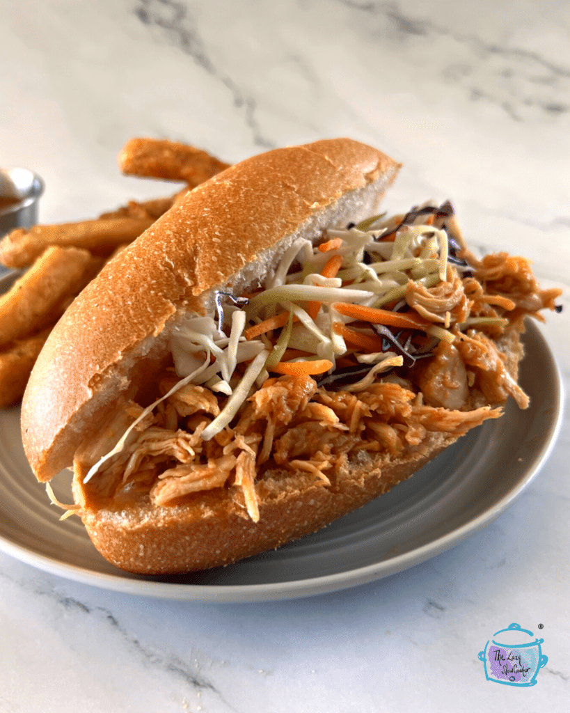 a sandwich made of slow cooker honey sriracha chicken and cabbage slaw viewed from the side