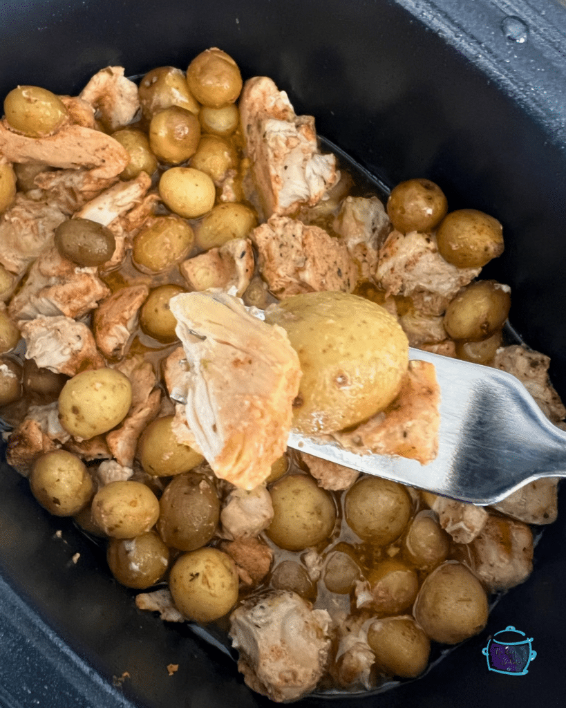 chicken on a fork over slow cooker filled with the same
