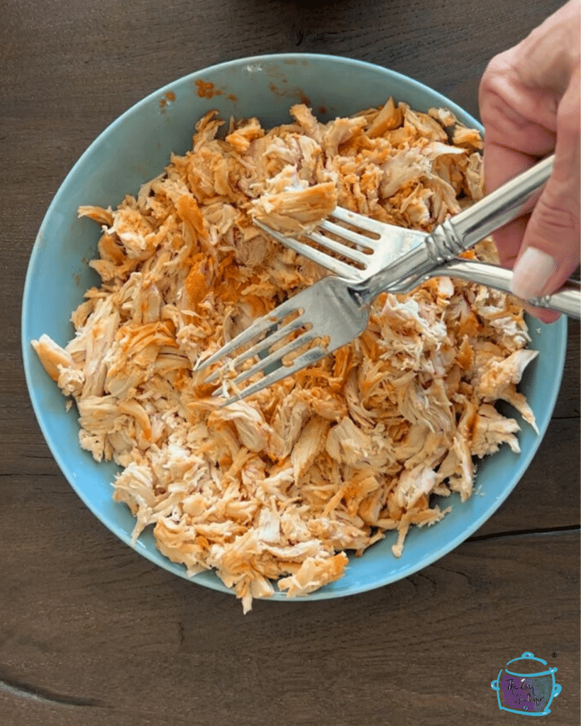 cooked chicken breasts being shredded with two forks