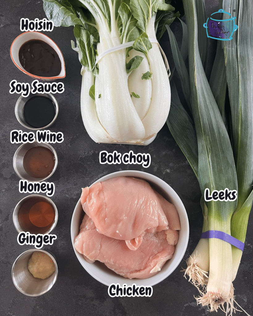 Overhead shot of Slow Cooker Chicken and bok choy ingredients: raw chicken breasts, bok choy, leeks, ginger, and labeled bowls of sauces and honey.