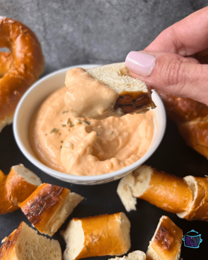 Slow cooker cheese and beer dip in a bowl with a soft pretzel being dipped