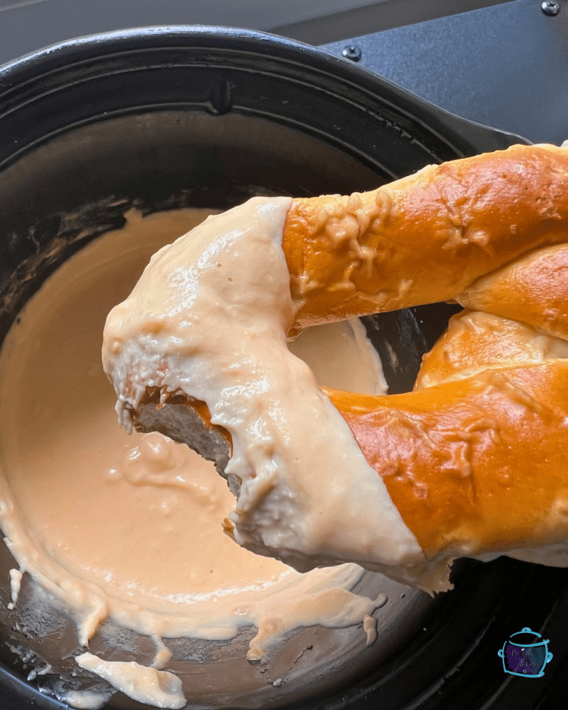 Slow cooker cheese and beer dip in a slow cooker with a soft pretzel being dipped